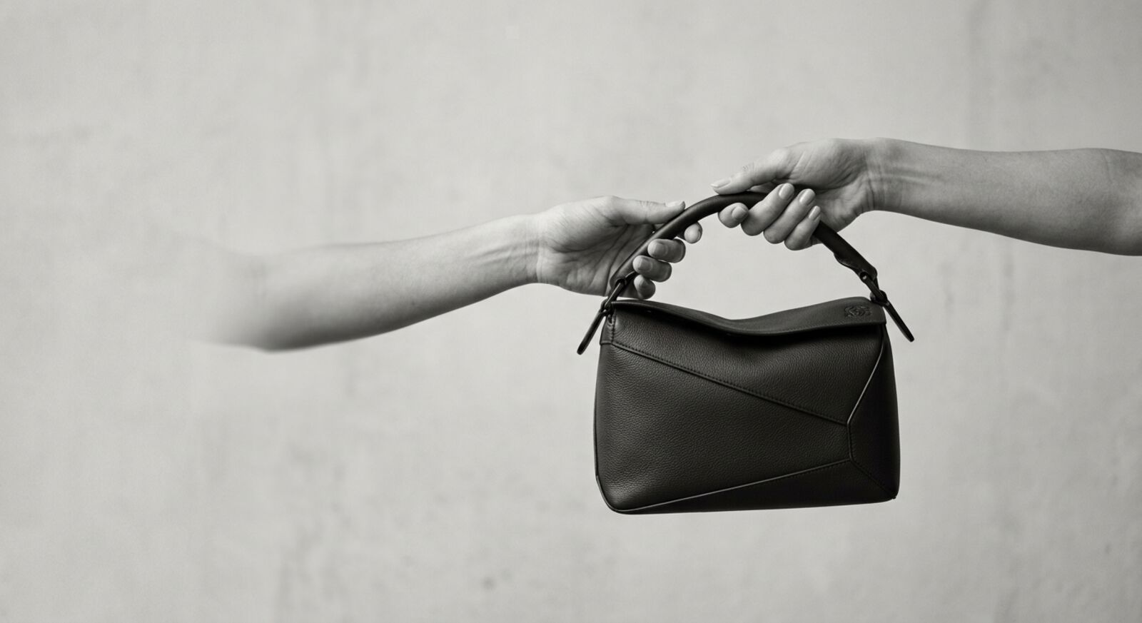 Two hands passing a designer handbag between strangers