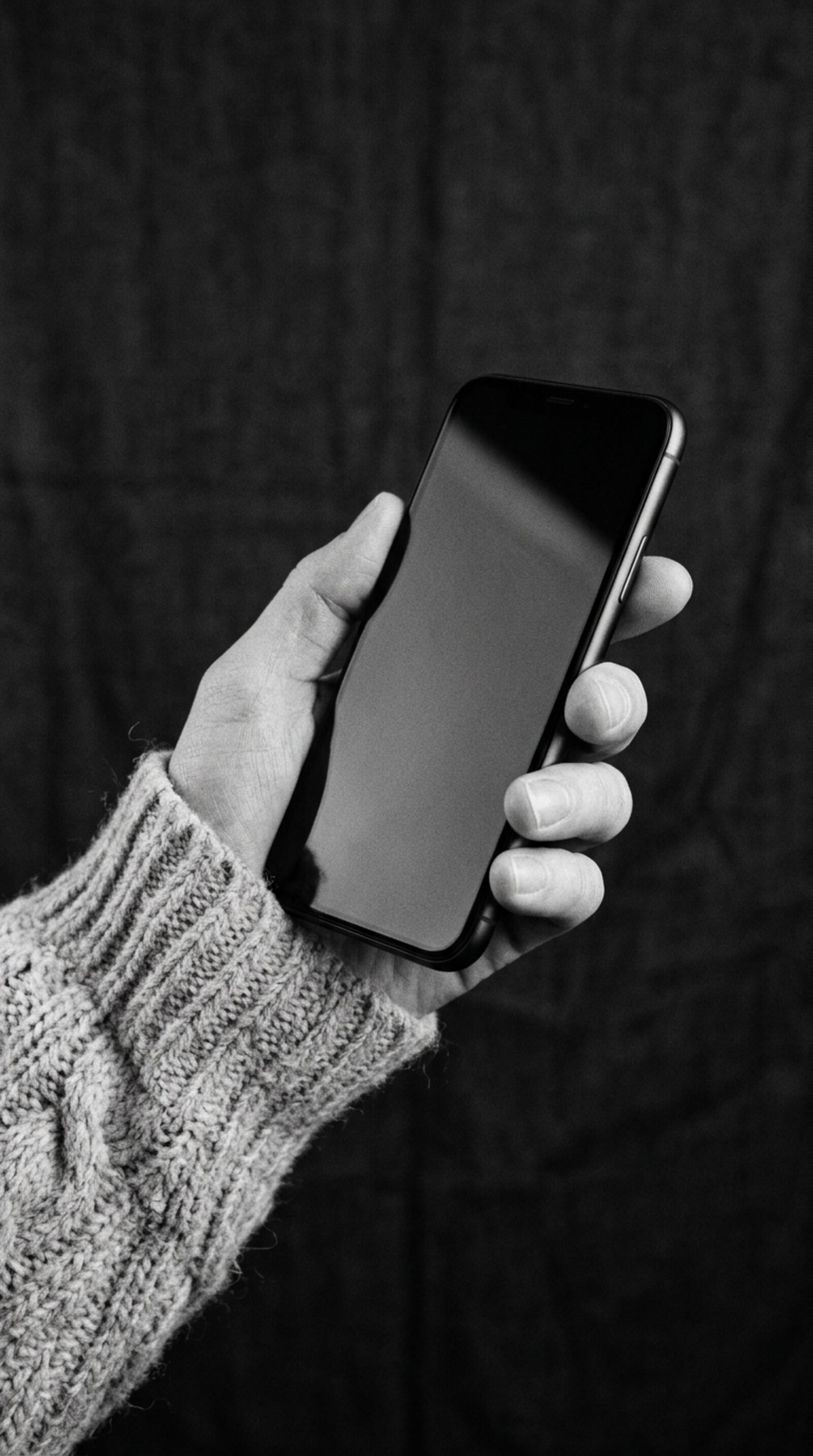 A hand in a knit sleeve holding a phone